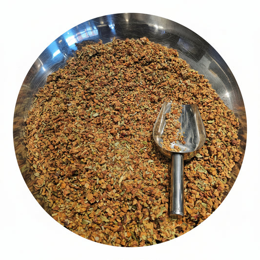 Metallic scoop in a bowl filled with dried herbs on a white background